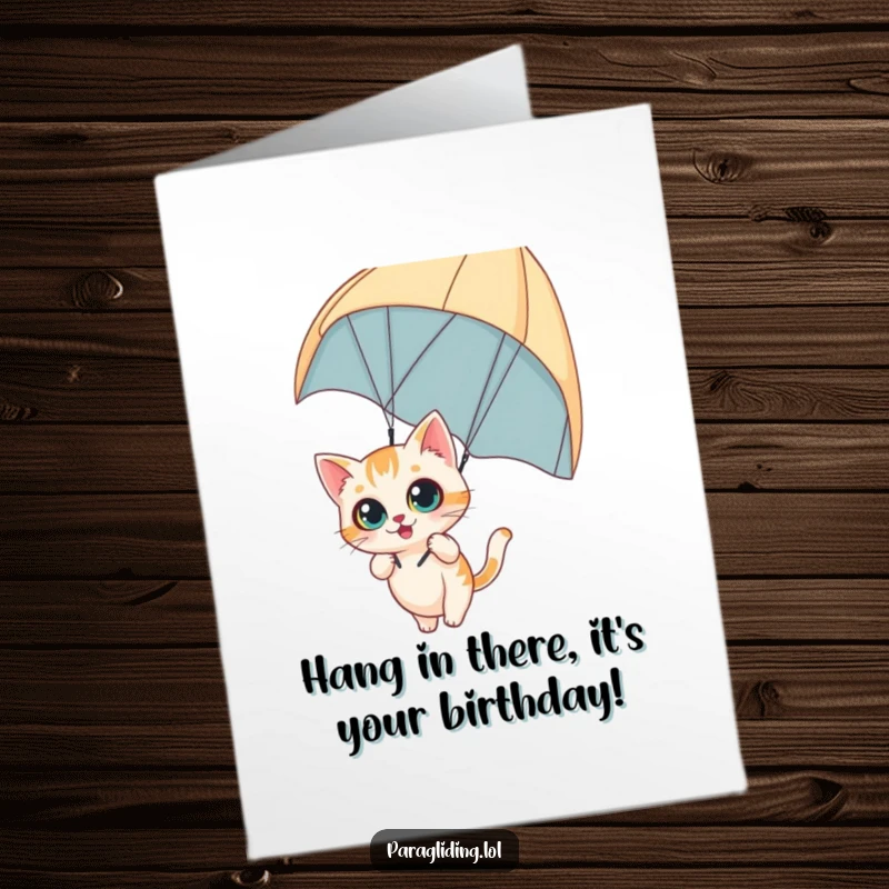 Funny Free Printable Birthday Card featuring a curious cat with wide eyes, comically dangling from a paraglider.
